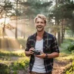 Man Holding a Vintage Camera in Forest Sunbeams