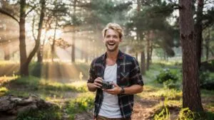 Man Holding a Vintage Camera in Forest Sunbeams