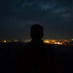 Man Looking at Distant Night Lights