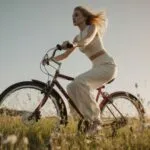 Margot Robbie spinning a bicycle wheel in meadow