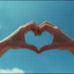 Two Hands Forming A Heart Against Blue Sky